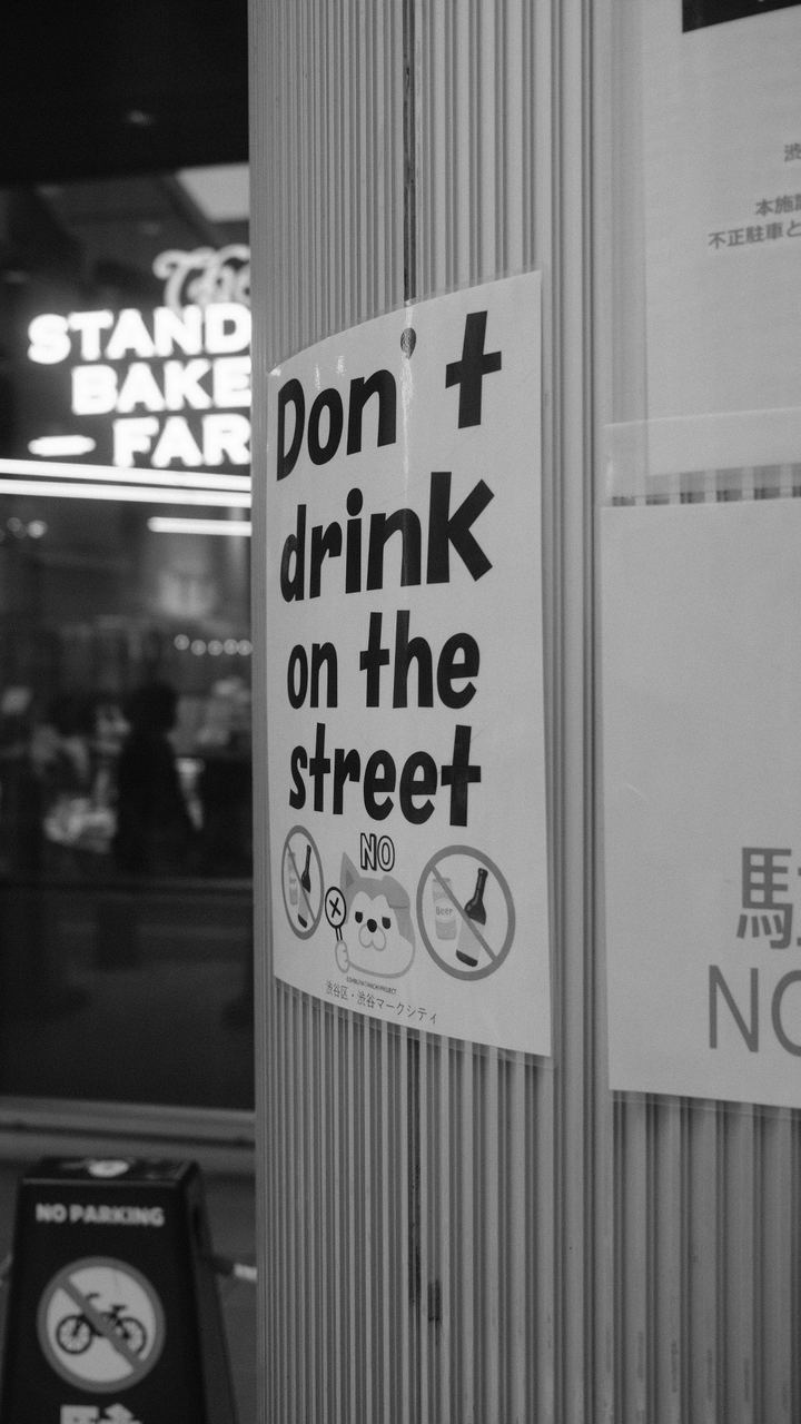 A hand-lettered 'don't drink on the street' sign on a fluted column, black and white, Shibuya