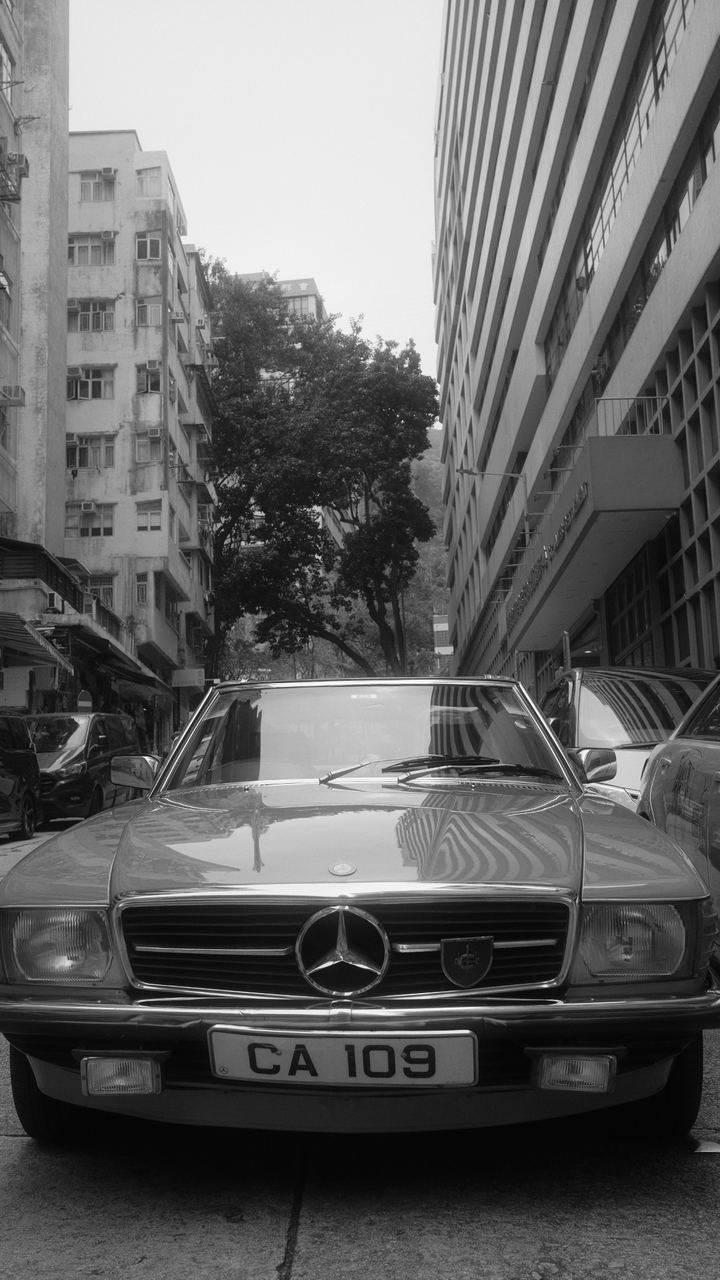 A vintage Mercedes coupe parked on a Hong Kong street, black and white