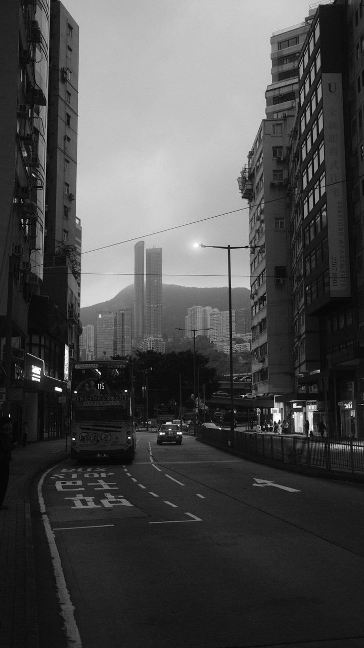 A double-decker bus on a misty Hong Kong avenue below the peak, black and white