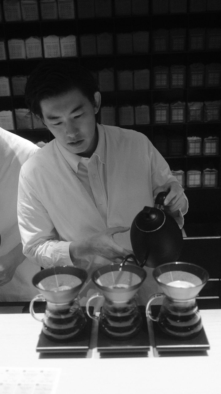 A man in a white shirt pouring three pour-over coffees, black and white, Tokyo