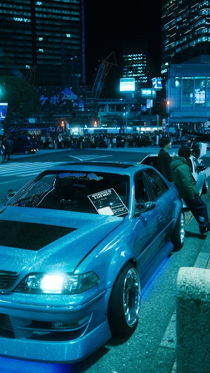 A tuned blue coupe at a night car meet under Shibuya's towers, Tokyo