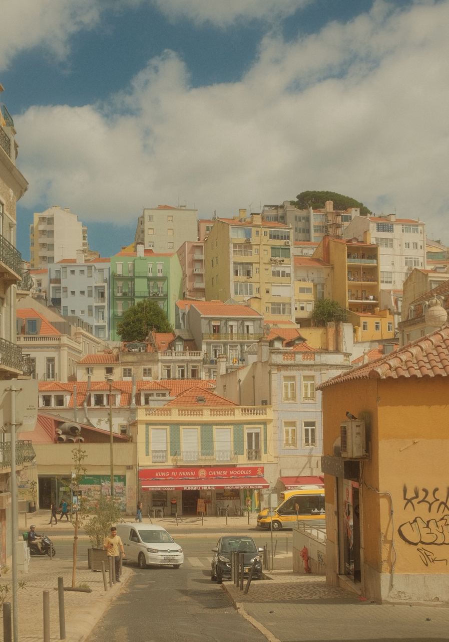 Pastel apartment blocks stacked up a Lisbon hillside above a noodle shop, Portugal