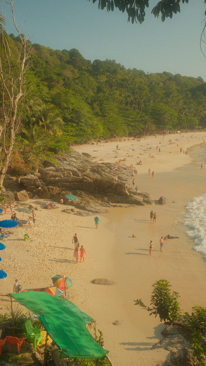 Sunbathers and umbrellas on a golden cove below jungle-covered hills, Thailand