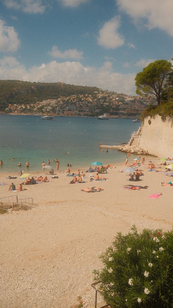 Swimmers and sunbathers on a pebble beach beside a turquoise bay, Villefranche-sur-Mer
