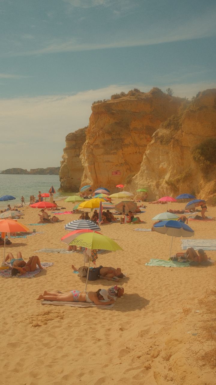 Sun umbrellas scattered across a golden Algarve beach below ochre cliffs, Portugal