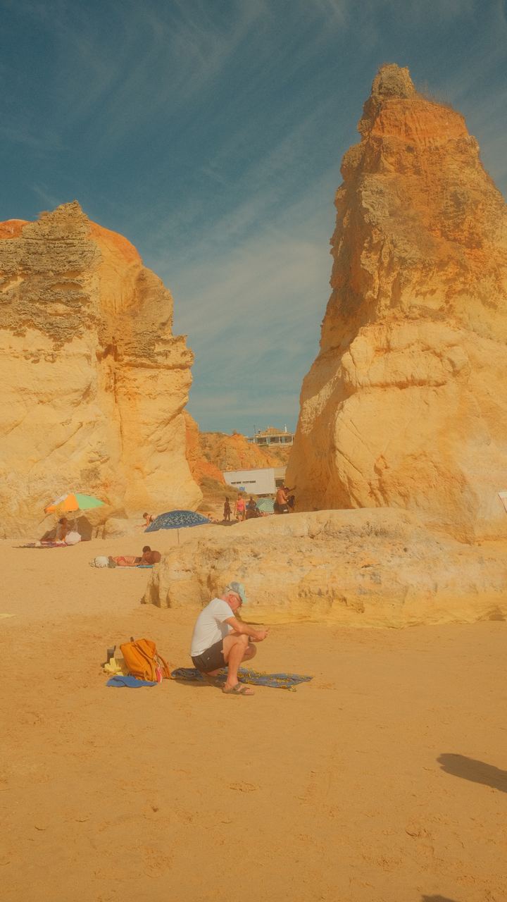 Beachgoers among towering golden rock stacks on an Algarve beach, Portugal